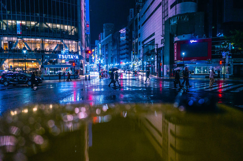 People on wet street in illuminated city at night during rain