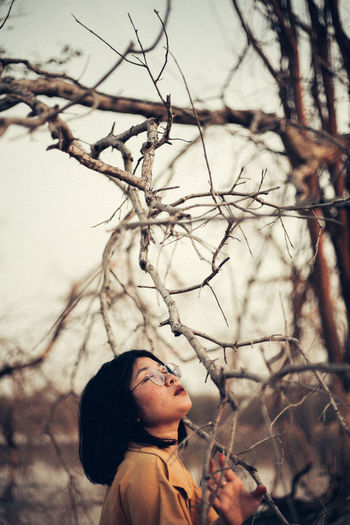 Portrait of young woman standing against bare tree