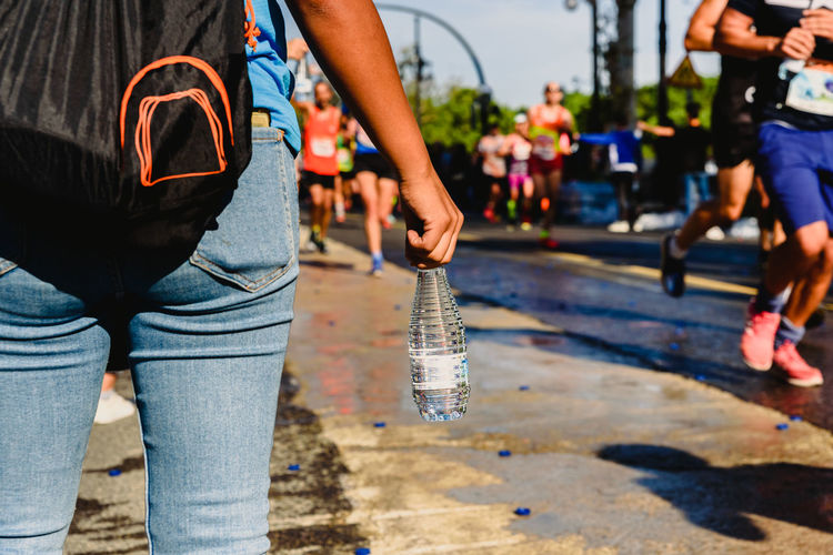Midsection of woman holding water bottle while standing on road