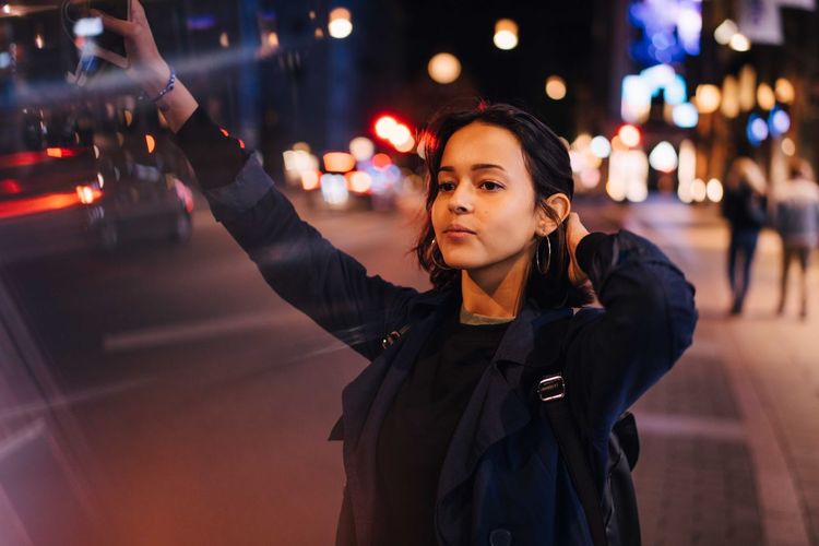 Young woman with hand in hair hailing for taxi in city at night