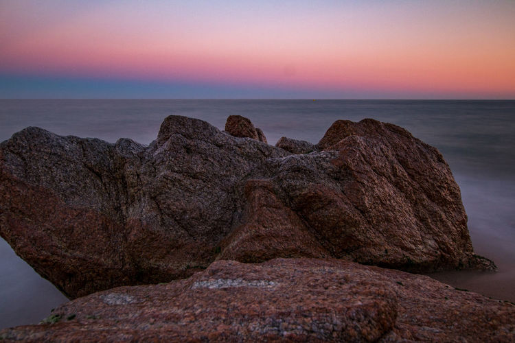 Rock formation on shore against sky during sunset