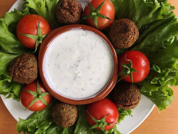 High angle view of falafels with cherry tomatoes and dip in plate on table