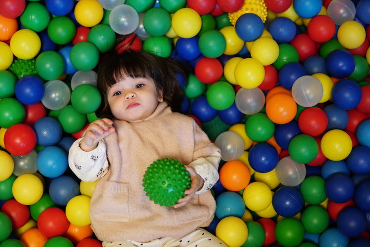 High angle view of cute baby girl looking away while lying on colorful balls