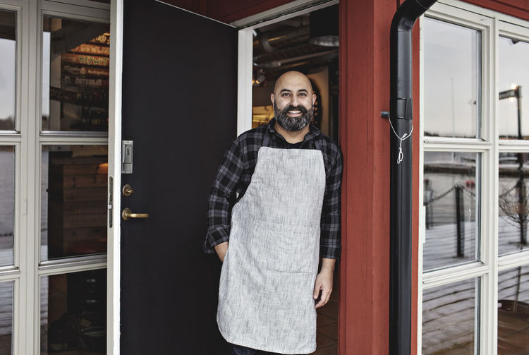 Portrait of smiling worker standing at doorway by restaurant