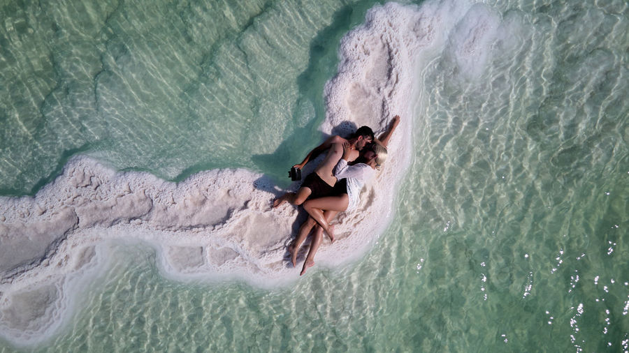 Couple of tourists rest and lie in an embrace on the shore of the dead sea
