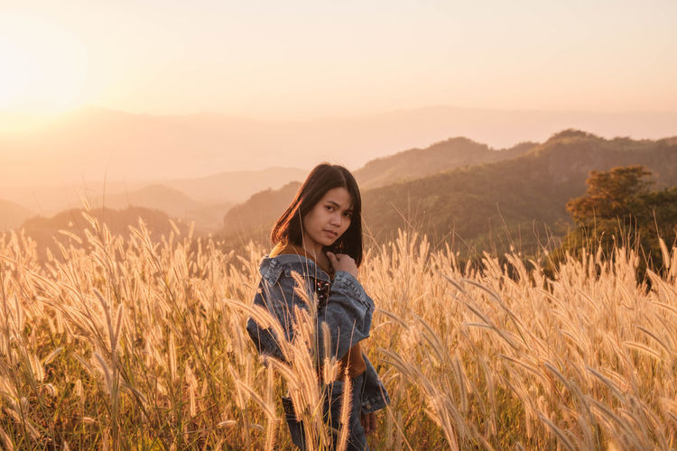 Portrait of young woman standing on field against sky during sunset