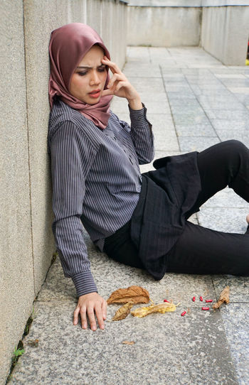 Full length of young woman sitting on sidewalk in city