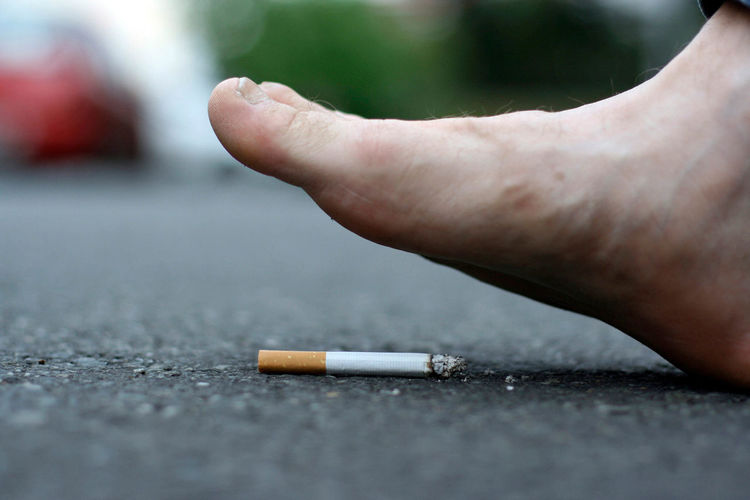 Close-up of human foot over cigarette on road