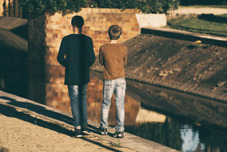 Rear view of siblings standing by canal
