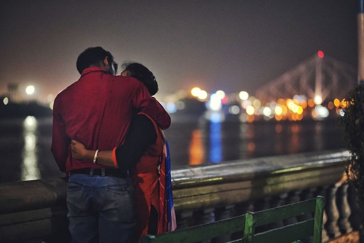 Couple kissing by railing against illuminated city at night