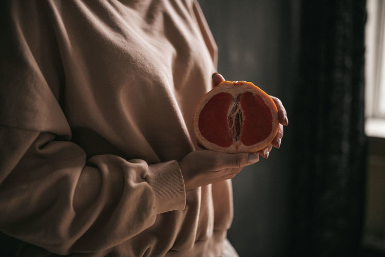 Midsection of woman holding grapefruit indoors