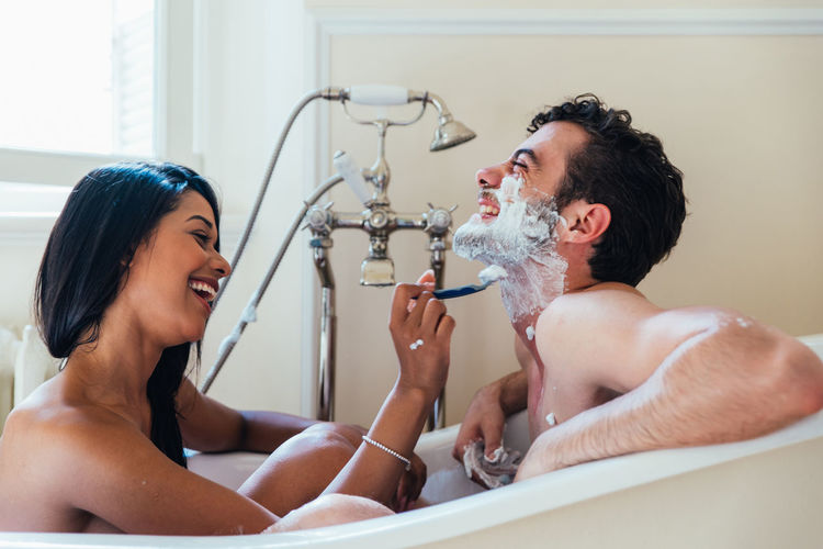 Woman shaving boyfriend while sitting in bathroom