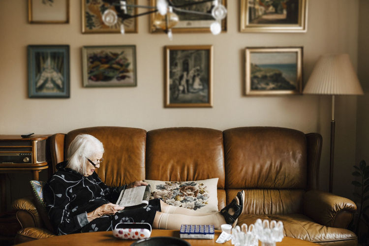 Senior woman reading newspaper while sitting on sofa in living room