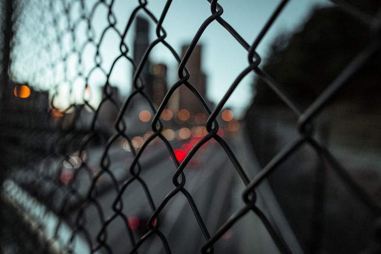 Close-up of chainlink fence against cityscape