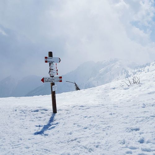 Sign board on snow covered mountain against cloudy sky