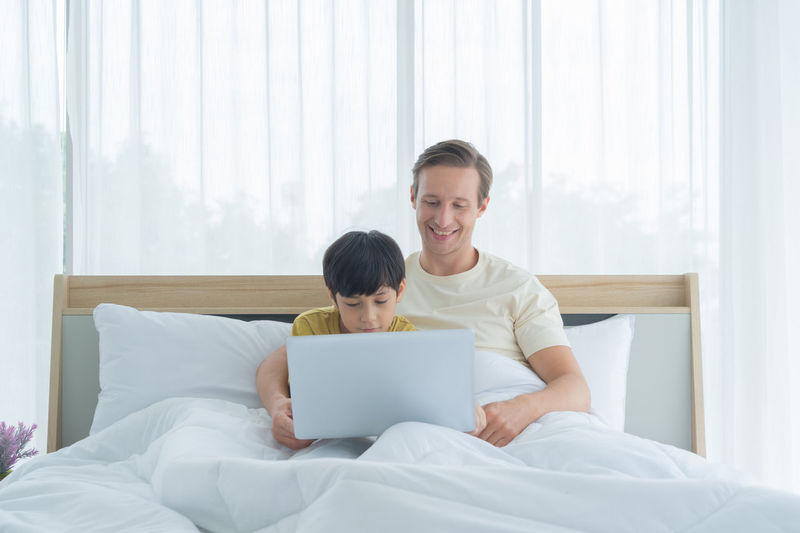 Man and woman using mobile phone while sitting on bed