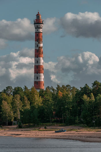 Lighthouse by trees and building against sky