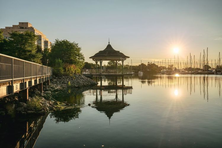 Built structure in lake by buildings against sky during sunset