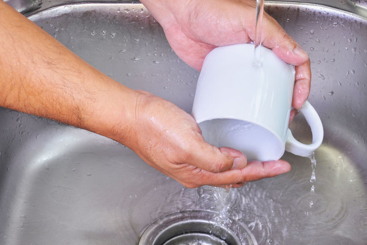 Cropped image of hands cleaning coffee cup in kitchen sink
