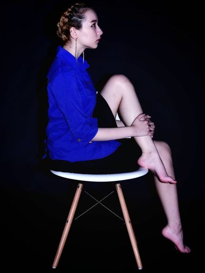 Woman sitting on chair against black background
