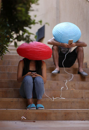 Friends wearing lanterns on head while using smart phones on steps