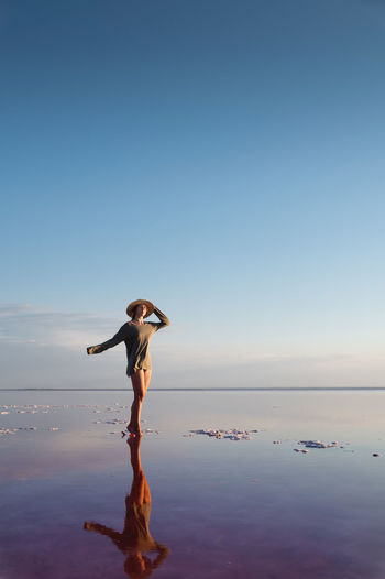 Young slender caucasian woman in a long sweater and a straw hat walking on tiptoes on a salt lake