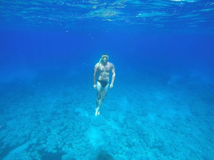 Full length of shirtless man swimming undersea