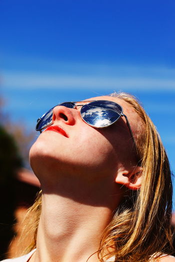 Young woman wearing sunglass looking up against sky