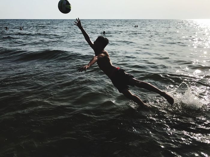 Boy jumping in sea against sky
