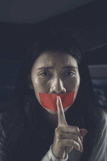 Close-up portrait of young woman gesturing over tape on mouth in darkroom