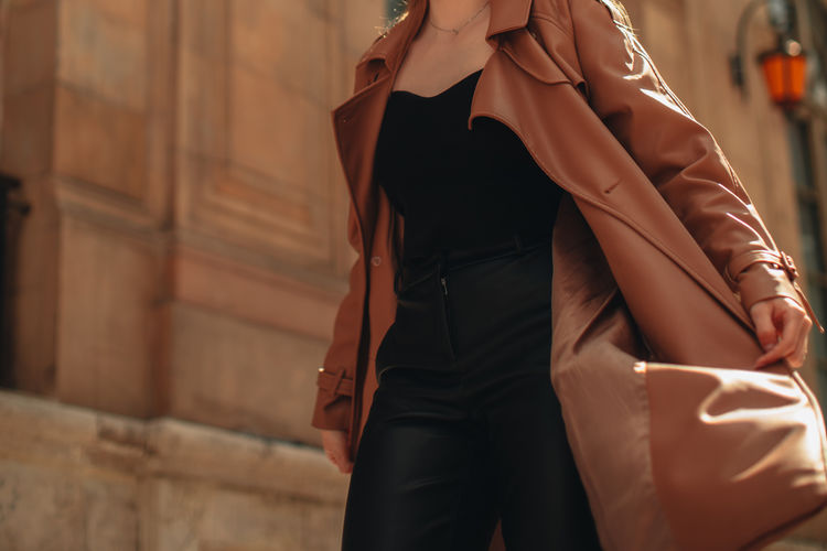 Cropped figure of young woman wearing stylish brown overcoat and black outfit. street casual