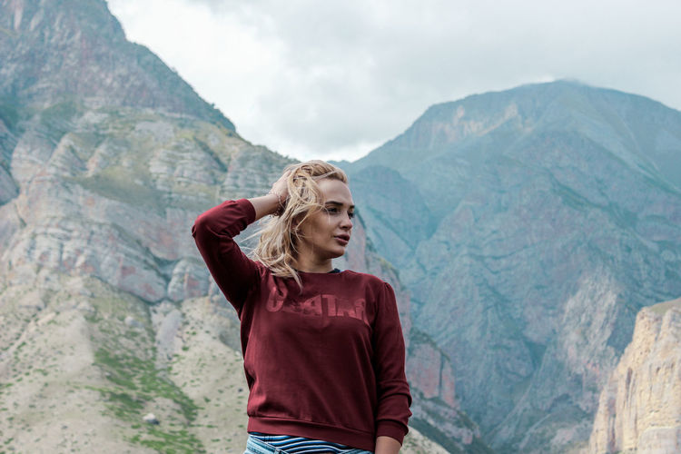 Young woman looking away while standing against mountain range