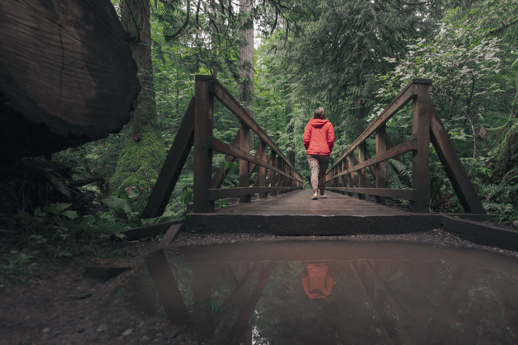 Woman crossing wooden bridge next to puddle in douglas forest