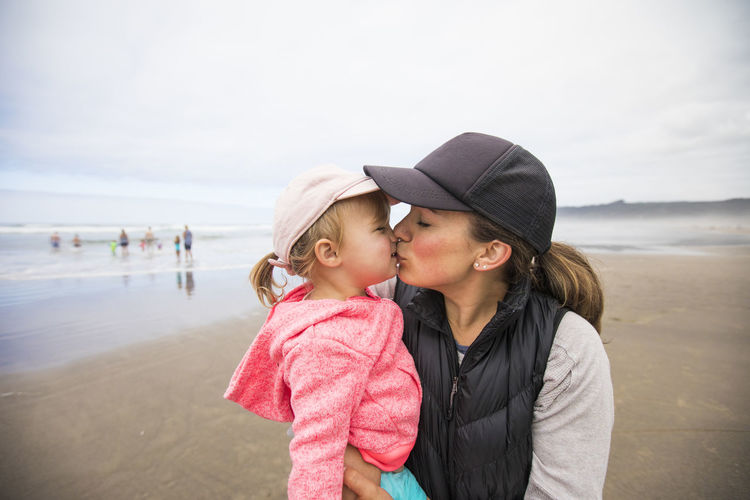 Mother gives daughter big kiss while at the beach.