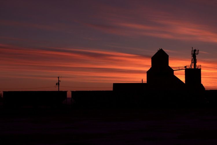 Silhouette train and grain elevator against sky during sunset