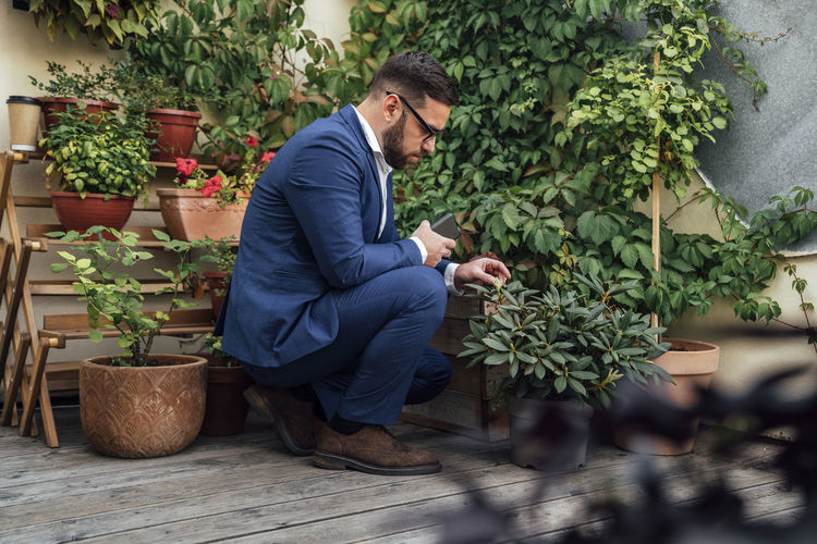 Side view of young man sitting by potted plants