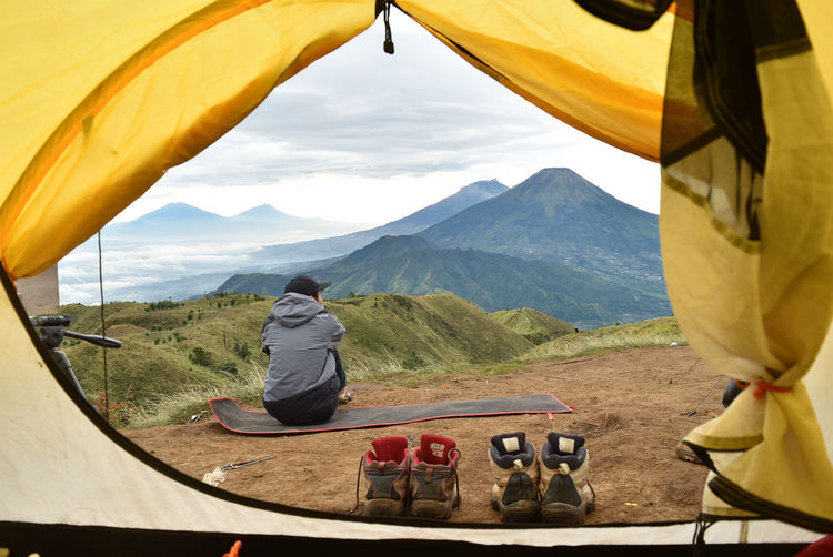 Rear view of man looking at mountains seen through tent