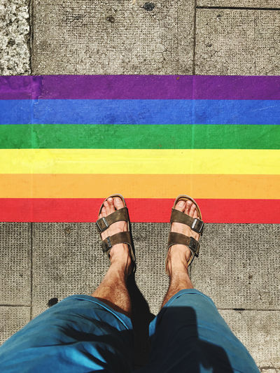 Low section of man standing by rainbow flag on footpath
