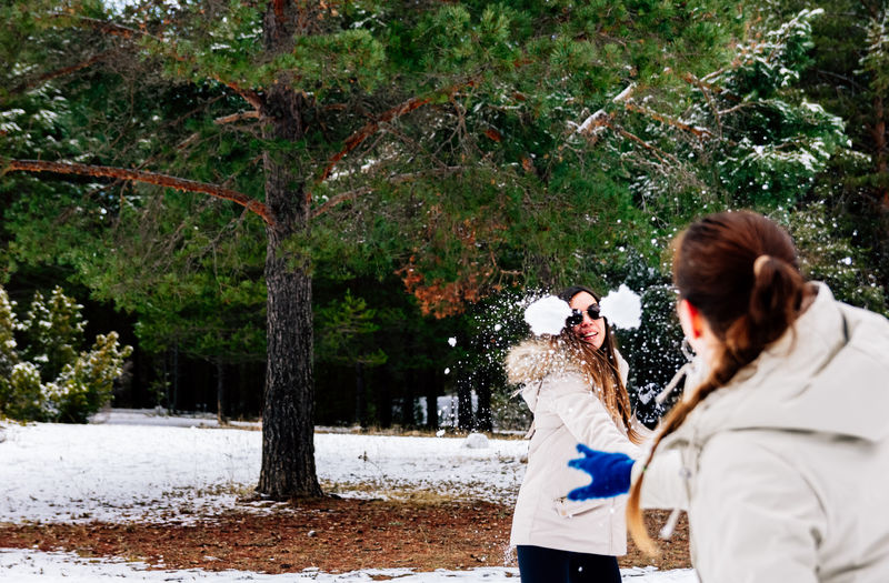 Rear view of woman playing snow fight with friend during winter