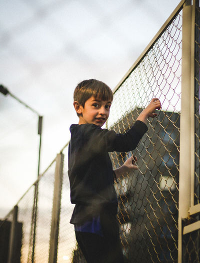 Portrait of boy standing by chainlink fence