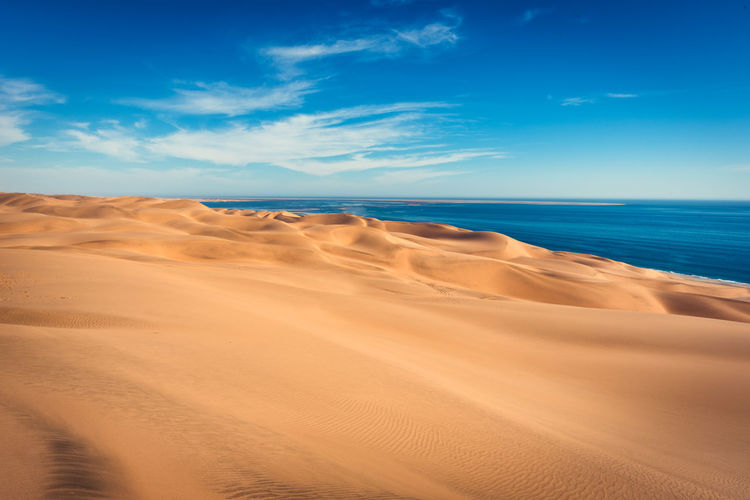 Scenic view of sand dunes by sea against blue sky