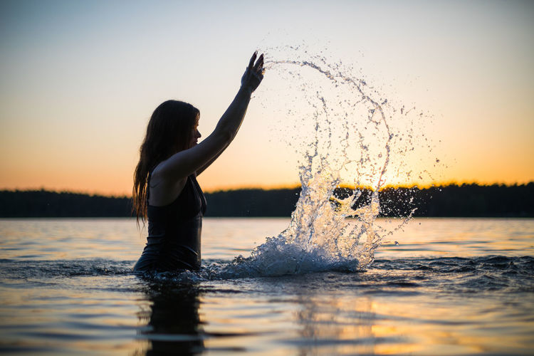 Beautiful girl in a long black swimsuit swims on the lake in the rays of sunset or dawn