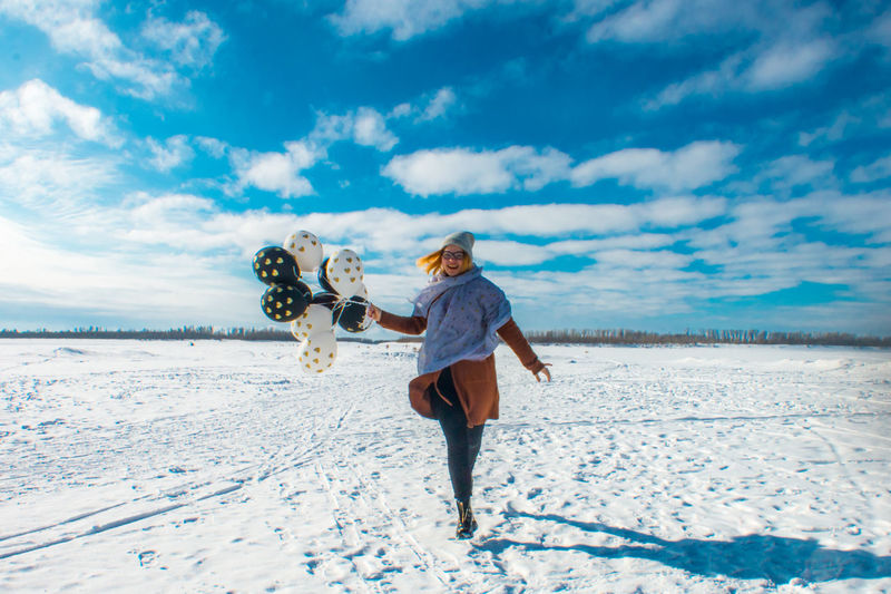 Woman with balloons walking on snow against sky
