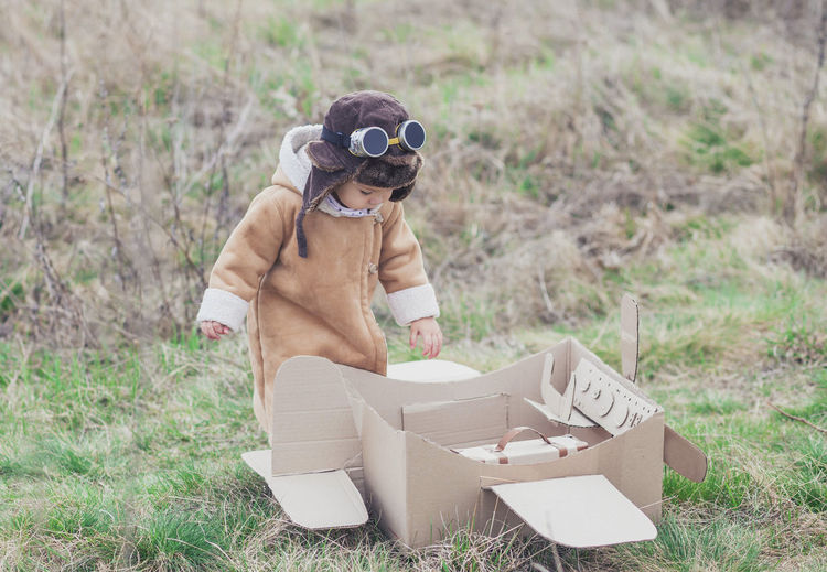 Charming baby in aviator's clothes gets on the cardboard plane