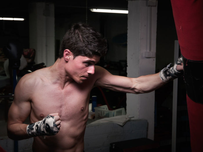 Shirtless man punching bag in boxing rink