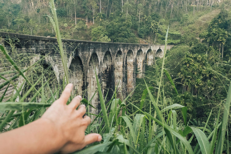 Crop anonymous male tourist exploring aged stone viaduct nine arch bridge located amidst green hillsides during trip in sri lanka