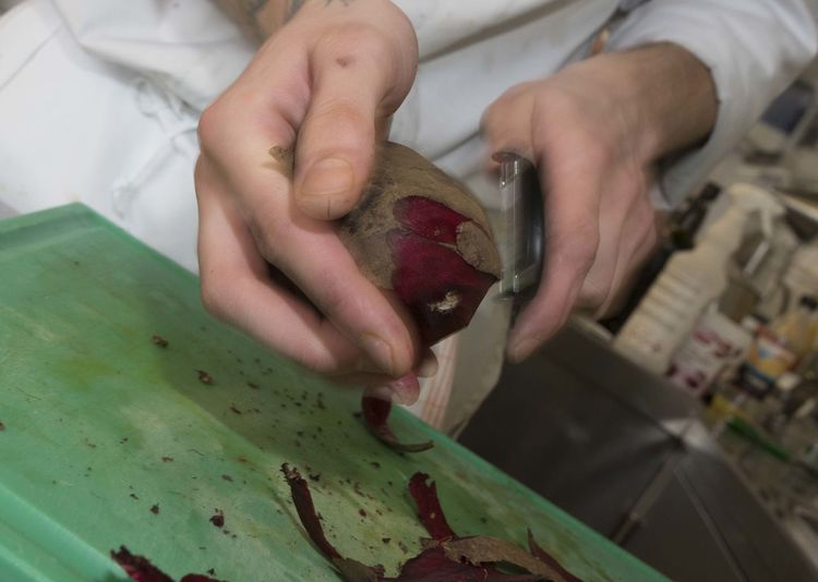 Cook is peeling beetroots with a peeler in the kitchen