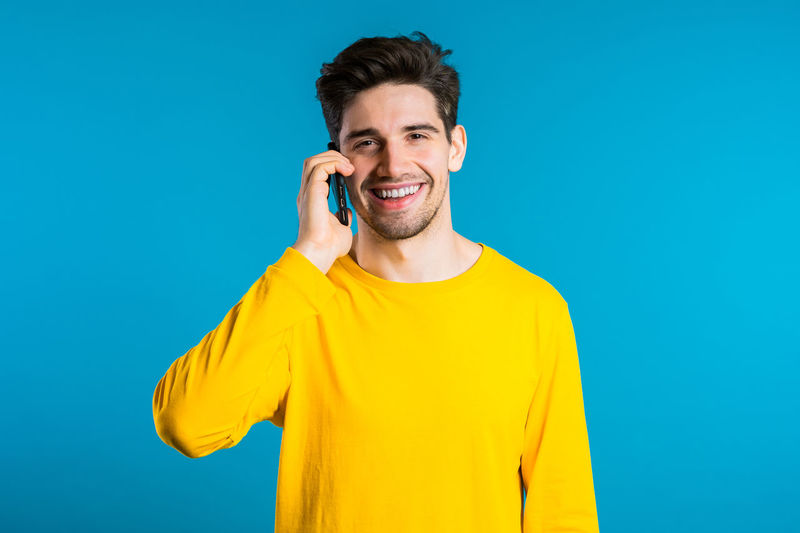 Portrait of smiling young man using smart phone against blue background