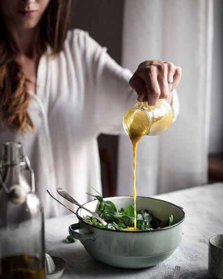 Midsection of woman pouring sauce in salad bowl