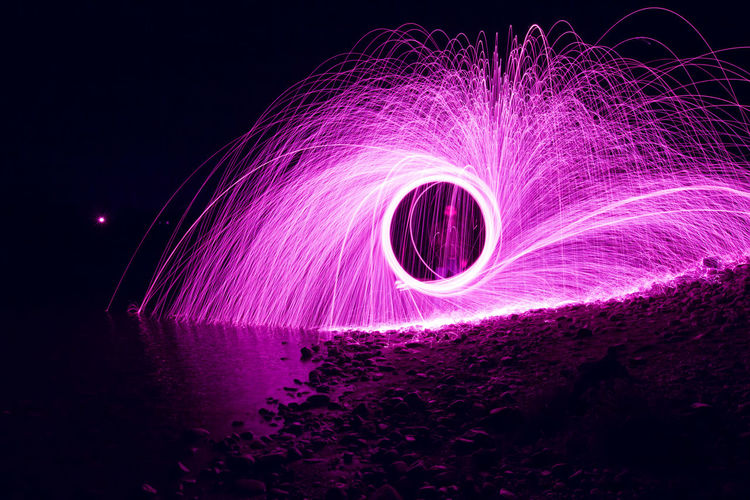 Man seen through spinning wire wool at beach during night